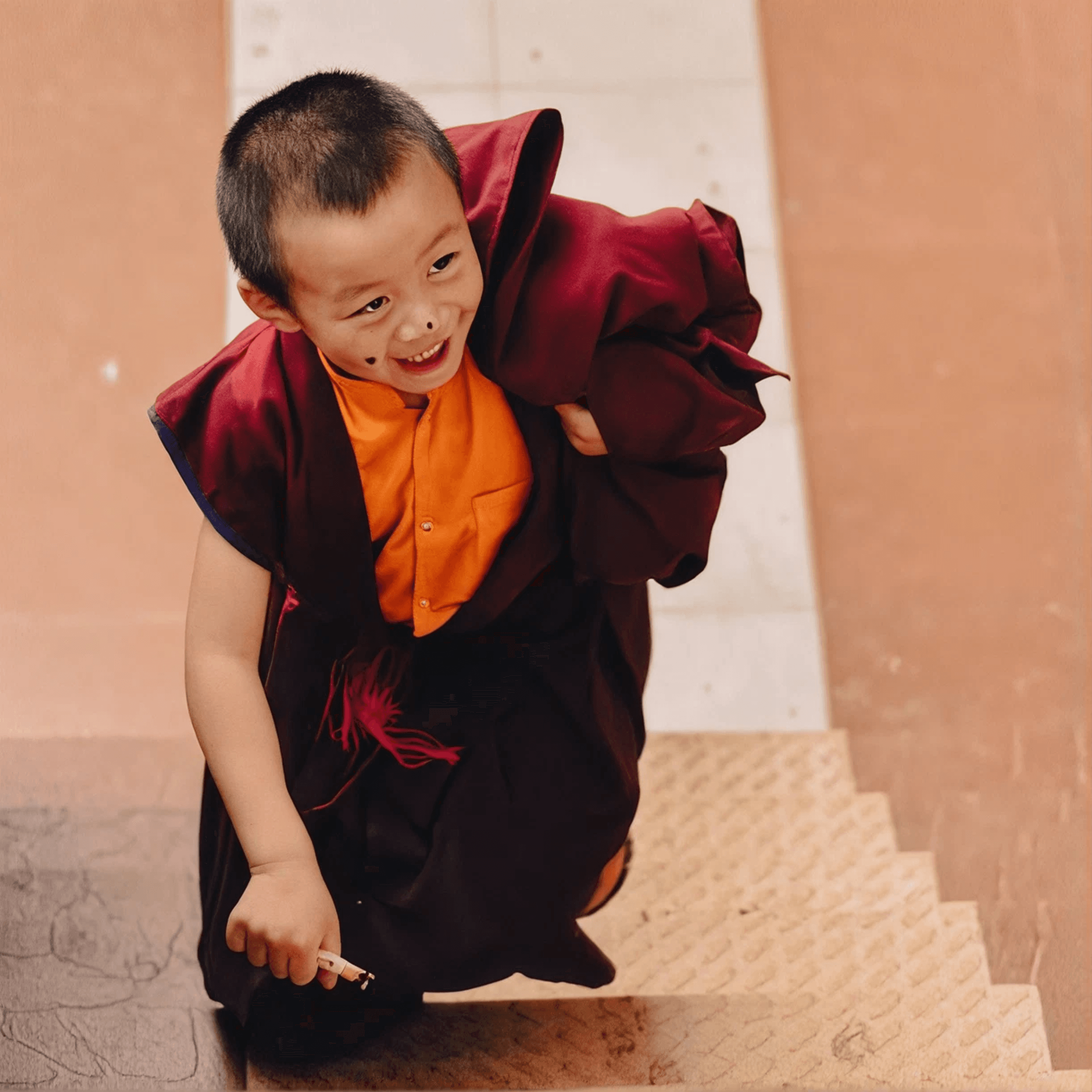 A young monk in maroon robes descending a stone staircase