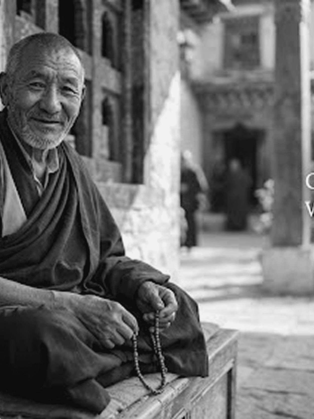 An elderly monk seated with prayer beads in a monastery courtyard